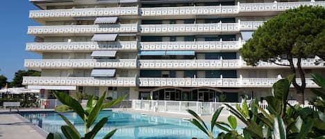 Un hôtel à plusieurs étages, doté de balcons, d’une piscine et d’un arbre au premier plan.