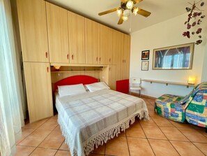 A bedroom with a bed, a ceiling fan, a chair, and a wall with a picture.