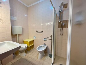 A bathroom with a toilet, bidet, sink, and shower.
