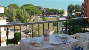Ein Balkon mit Esstisch, der auf eine Küstenlandschaft mit Gebäuden und Bäumen blickt.