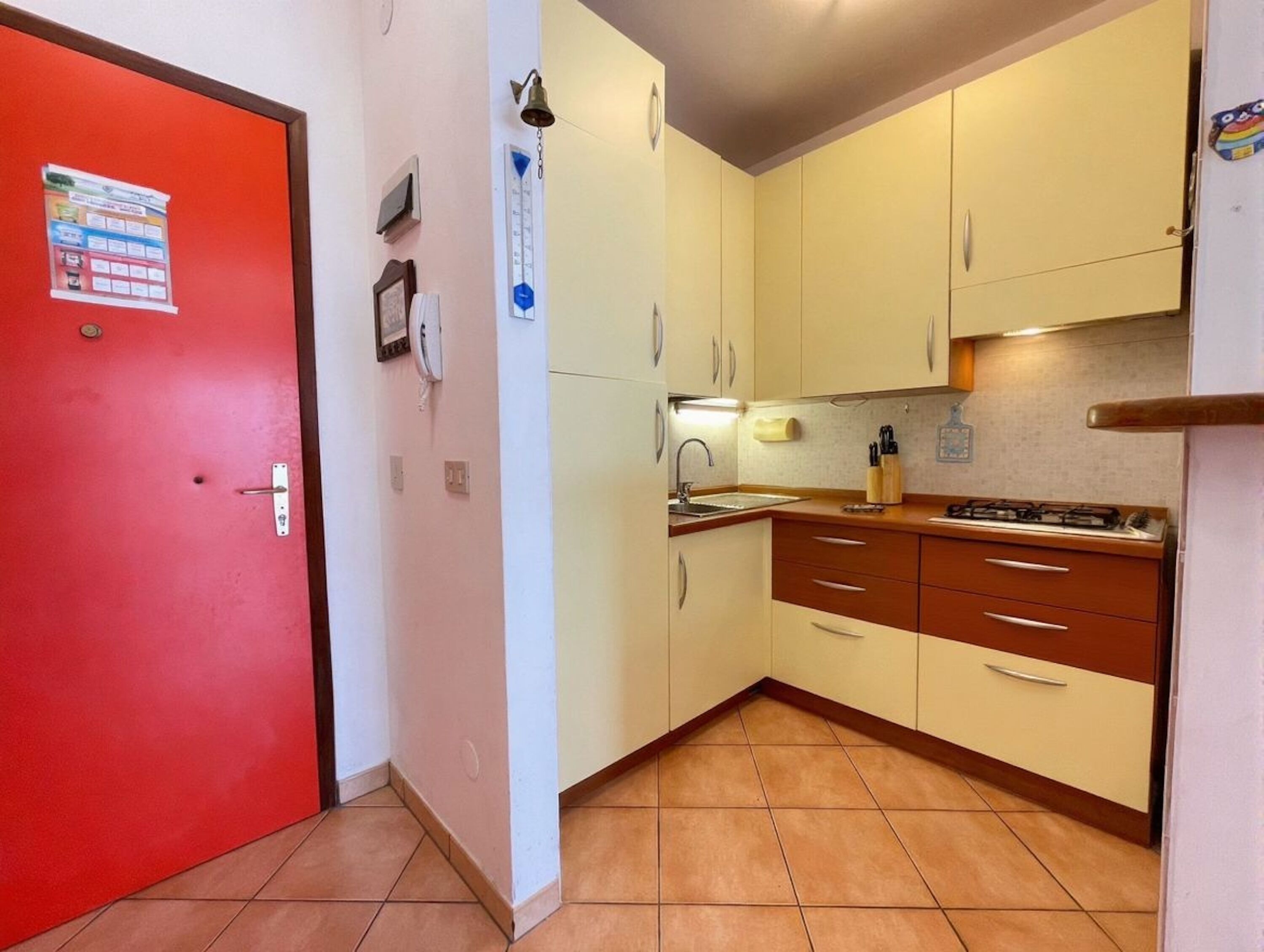 Une cuisine de taille réduite avec une porte rouge, des murs blancs et un sol carrelé.