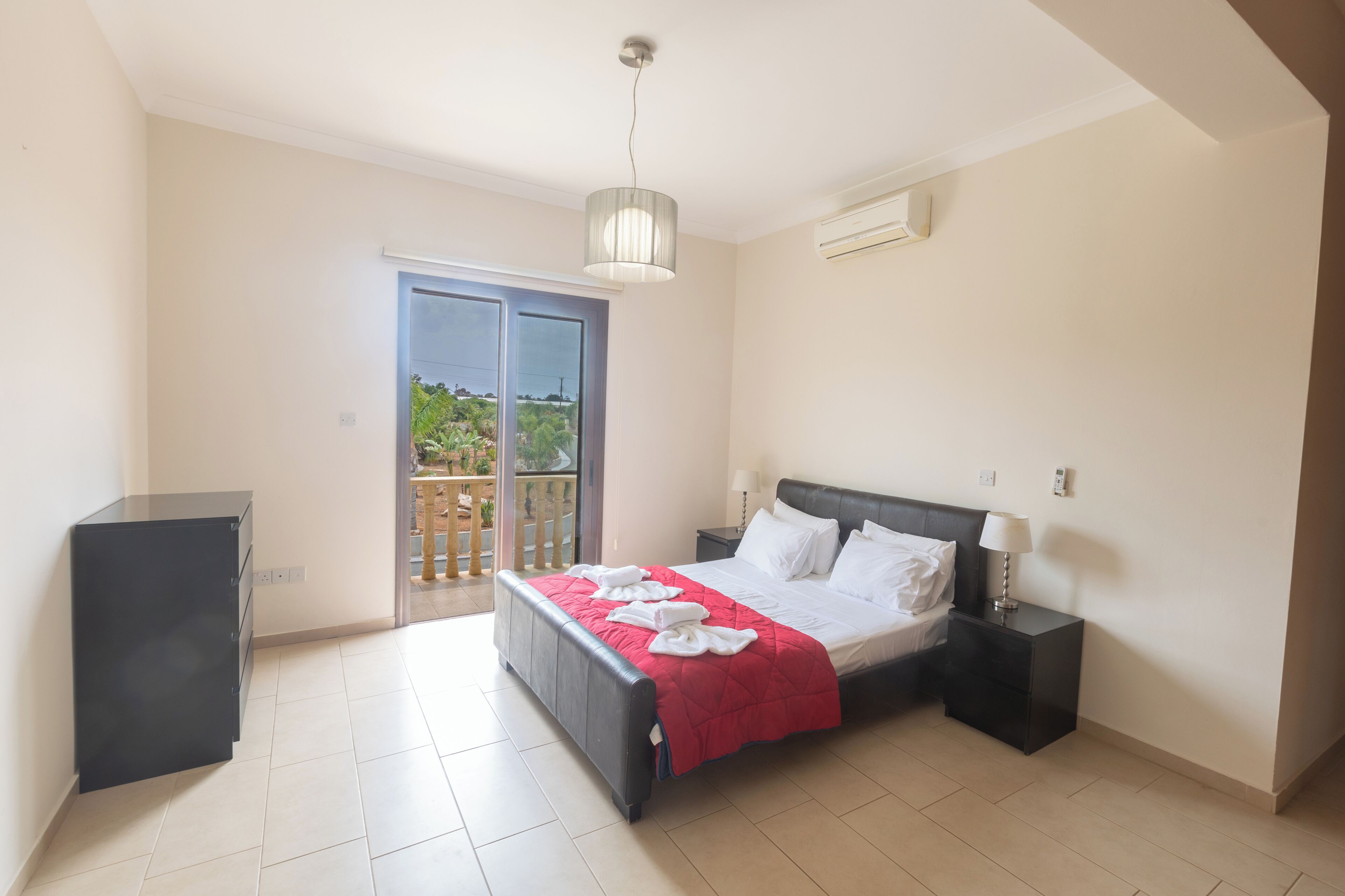 A bedroom with a bed, bedside tables, a wardrobe, and a balcony with a view.