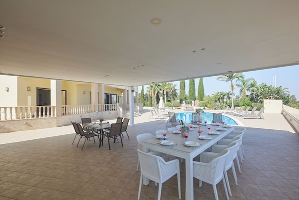 A covered outdoor dining area with a pool in the background.