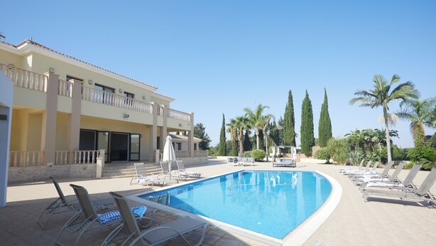 A swimming pool with lounge chairs and a building with balconies. - Protaras Holiday Villa Pa7 Private 7 Bedroom Villa (Paralimni)
