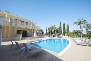 A swimming pool with lounge chairs and a building with balconies. - Protaras Holiday Villa Pa7 Private 7 Bedroom Villa (Paralimni)