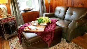 En hyggelig stue med en lædersofa, et lille træsidebord med en lampe, og et bakke med en bog, blomster og en tallerken.