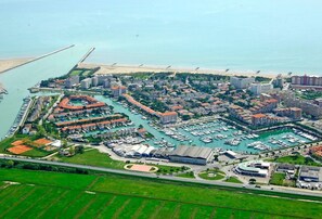 An aerial view of a coastal marina with multiple docks, a large parking area, and surrounding residential buildings. - Beautiful Apartment For 5 People-swimming Pool-ac by Beahost Rentals (Caorle)