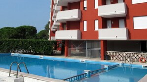 A multi-story building with balconies, a swimming pool, and a tiled border. - Cozy Flat Close to the sea (Caorle)
