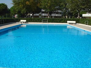 Ein rechteckiger Swimmingpool mit klarem, blauem Wasser, umgeben von einer niedrigen weißen Mauer und einem Heckenstreifen.