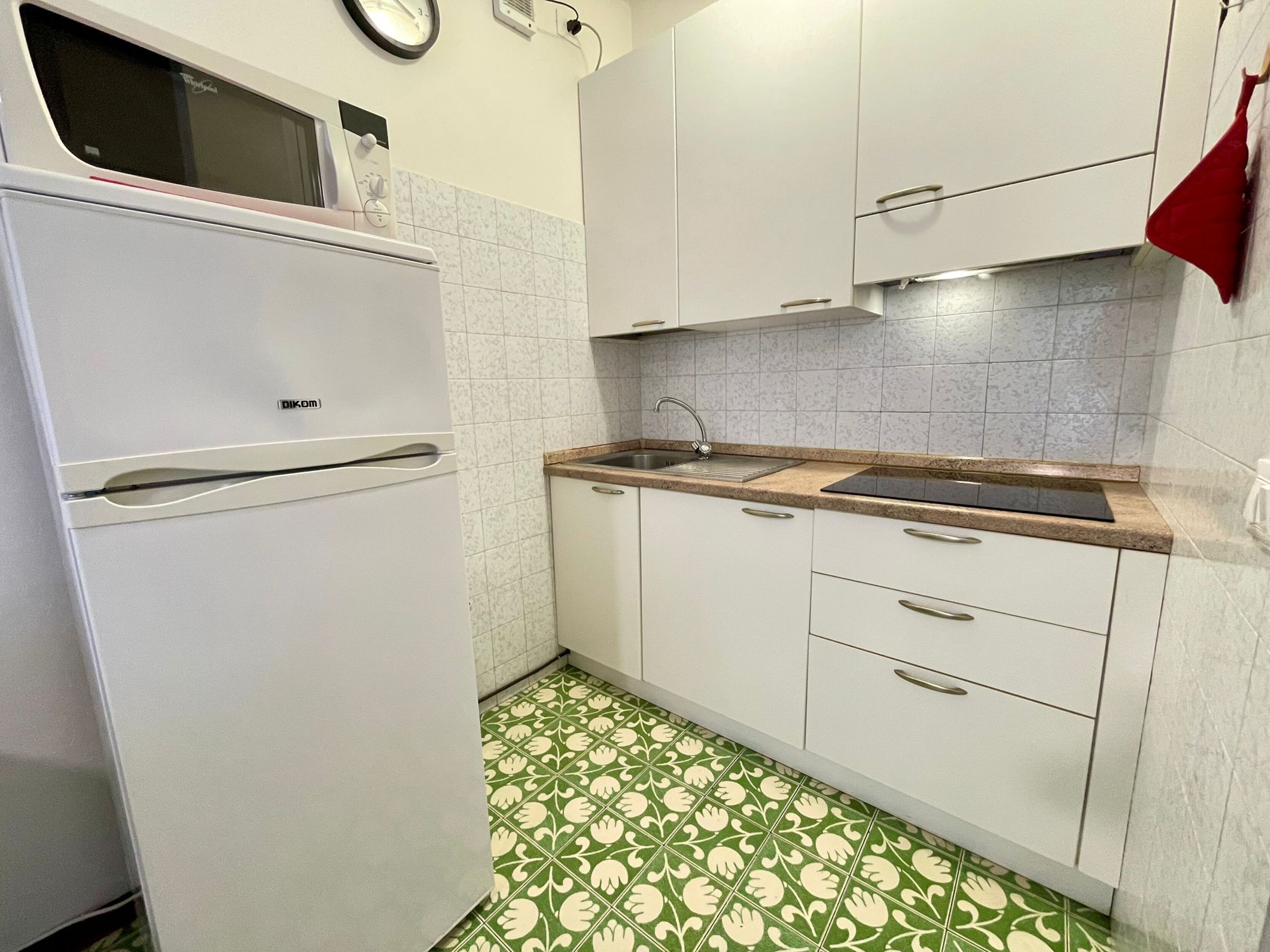 A compact kitchen with white cabinets, a sink, and a patterned floor.