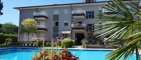 A modern apartment building with a swimming pool, balconies, and a well-maintained garden.