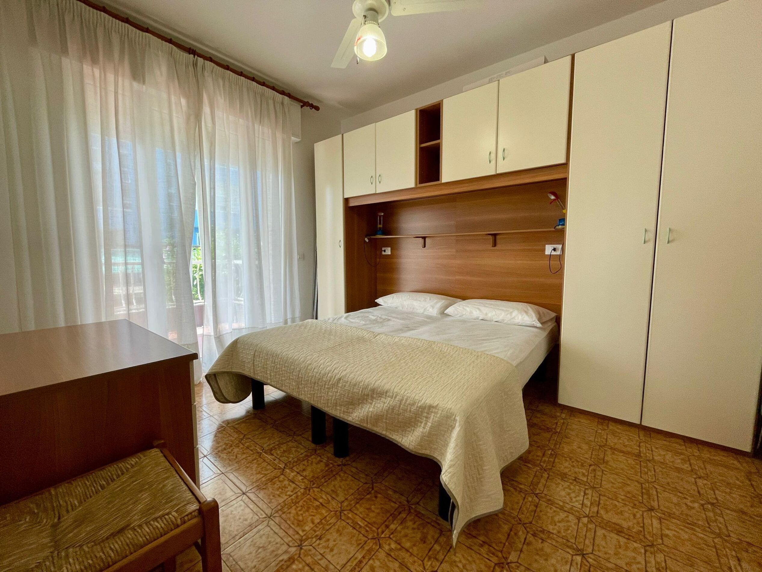 Un dormitorio con cama, cabecero de madera, armarios blancos, un escritorio y una silla.