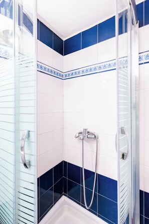Ein Duschbereich mit Glastür, weißen und blauen Fliesen und einer Handbrause.