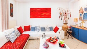 A modern living room with a white sofa, red and blue cushions, a red abstract painting, a vase with branches, and a small table with a plant and decorative items. - the Cosy Modern and Comfortable Apartment in the Heart of Heraklion City Centre (Heraklion)