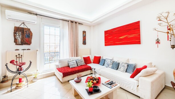 A modern living room with a white sofa, red cushions, a coffee table with decorative items, and a red abstract painting on the wall. - the Cosy Modern and Comfortable Apartment in the Heart of Heraklion City Centre (Heraklion)