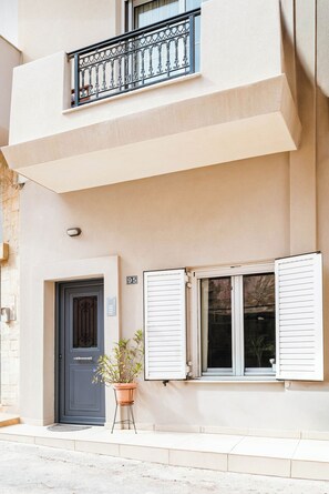 Ein Gebäude mit einer dunklen Tür, einem Balkon mit Metallgeländern und einem Blumentopf im Erdgeschoss.