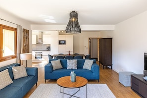 Un salon moderne avec un canapé bleu, une table basse en bois et un coin repas agrémenté d’un buffet en bois foncé.