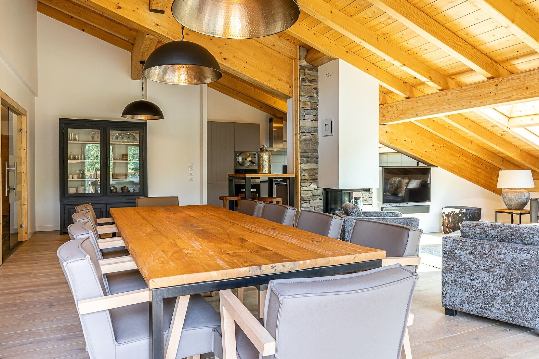 Un vaste espace dédié à la salle à manger, avec une longue table en bois et des chaises modernes, une cheminée en pierre et un coin salon confortable avec un canapé et des fauteuils.