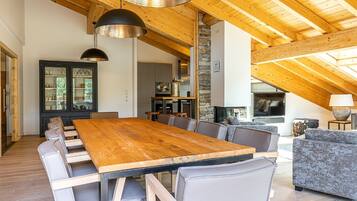 Un vaste espace dédié à la salle à manger, avec une longue table en bois et des chaises modernes, une cheminée en pierre et un coin salon confortable avec un canapé et des fauteuils.