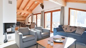 A spacious living area with a high wooden ceiling, a fireplace, a blue sofa, and a dining area with chairs and a table. - Chalet in French Alps near Lake Geneva (Abondance)