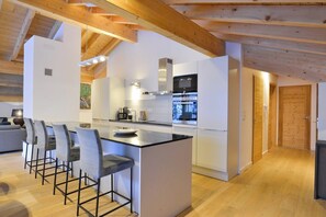 A modern kitchen with a central island, bar stools, and wooden beams. - Chalet in French Alps near Lake Geneva (Abondance)