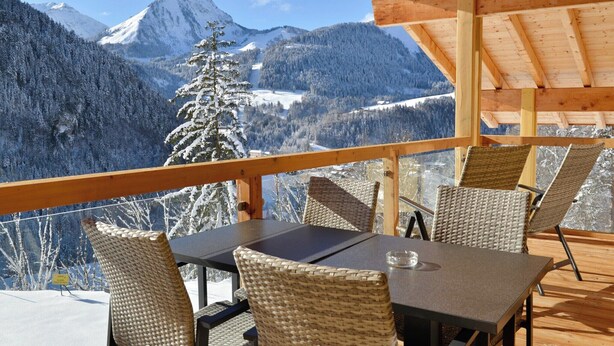 A wooden deck with a table and chairs overlooking a snowy mountain landscape. - Chalet in French Alps near Lake Geneva (Abondance)