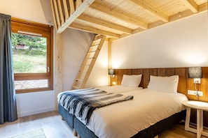 A bedroom with a bed, a window, a wooden ceiling, and a wall-mounted lamp.