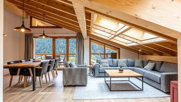 Un loft spacieux avec de hauts plafonds, des poutres apparentes, un coin repas avec une longue table et des chaises, un canapé et une table basse.