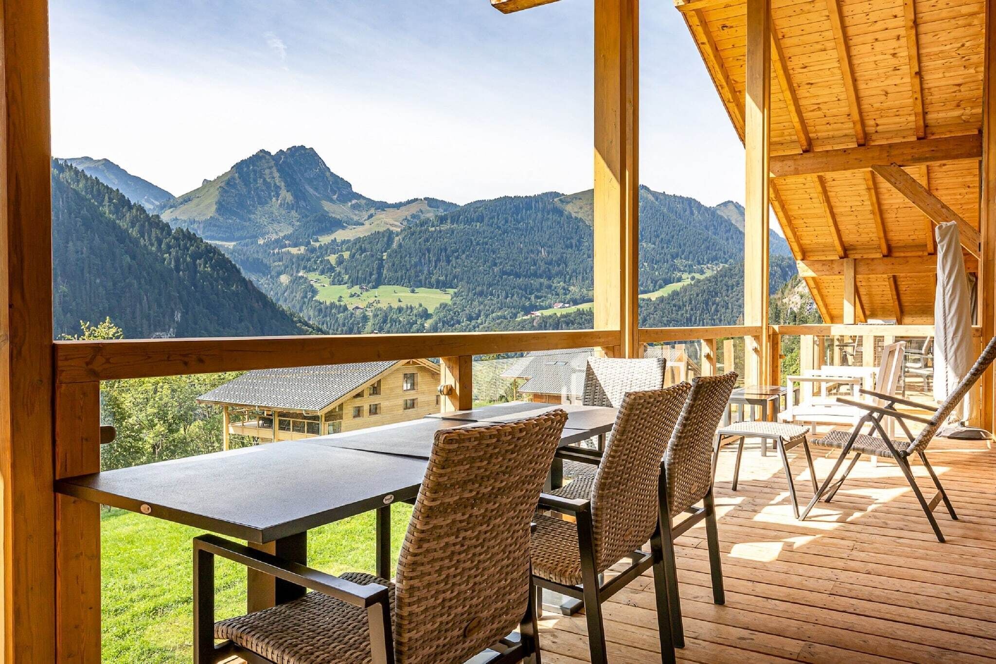 Une terrasse en bois avec une table et des chaises, offrant une vue sur un paysage montagneux.