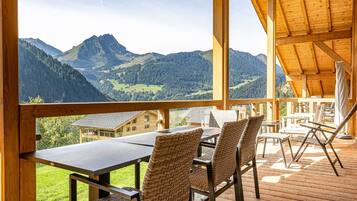 Une terrasse en bois avec une table et des chaises, offrant une vue sur un paysage montagneux.