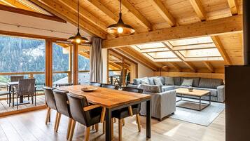 Une pièce spacieuse avec un plafond en bois, une table à manger avec des chaises, un canapé et une grande fenêtre donnant sur les montagnes.