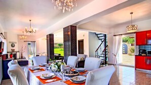 A dining area with a table set for four, a chandelier, and a view of the outdoors. - Luxury Endless Sea View Escape (Plaka)