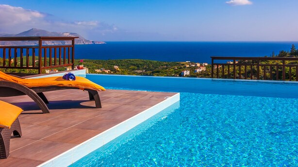 A poolside area with a view of the ocean and a mountain in the distance. - Luxury Endless Sea View Escape (Plaka)