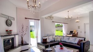 A spacious living area with a sectional sofa, a coffee table, a fireplace, and a view of the garden. - Luxury Endless Sea View Escape (Plaka)