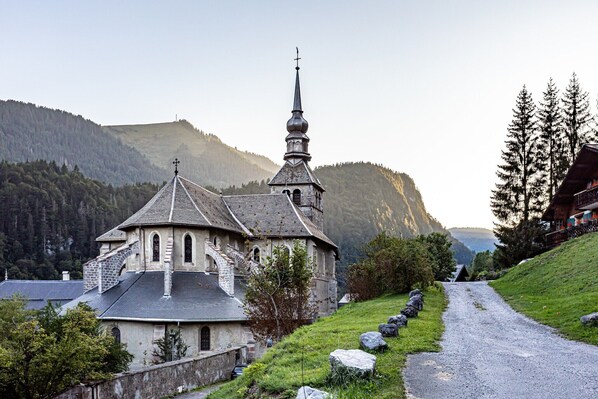 A church with a prominent steeple, surrounded by a rural landscape with a gravel path and a hillside.