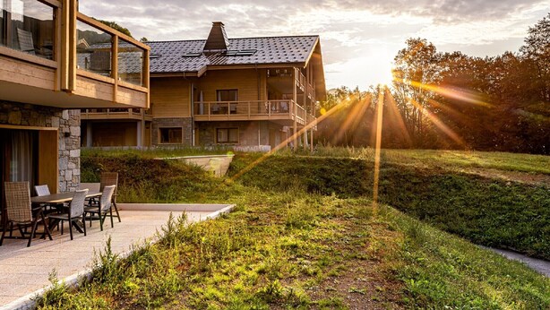 En moderne bygning i to etager med en stenfacade, en balkon og et spiseområde med udendørs møbler.