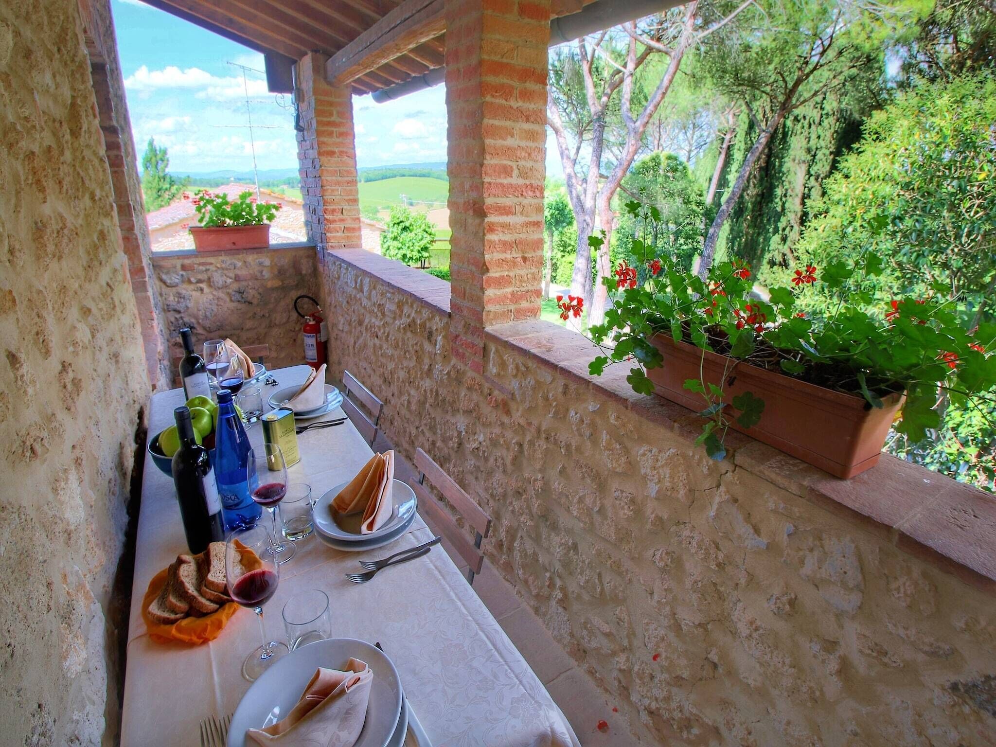 Une table dressée pour le dîner, avec des verres à vin, des bouteilles et des assiettes, donnant sur un jardin luxuriant agrémenté de plantes en pot et de fleurs.