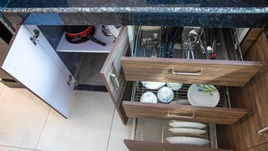 A kitchen with a dishwasher, open cabinets, and a tiled floor. - Whiteboard Homes (Siolim)