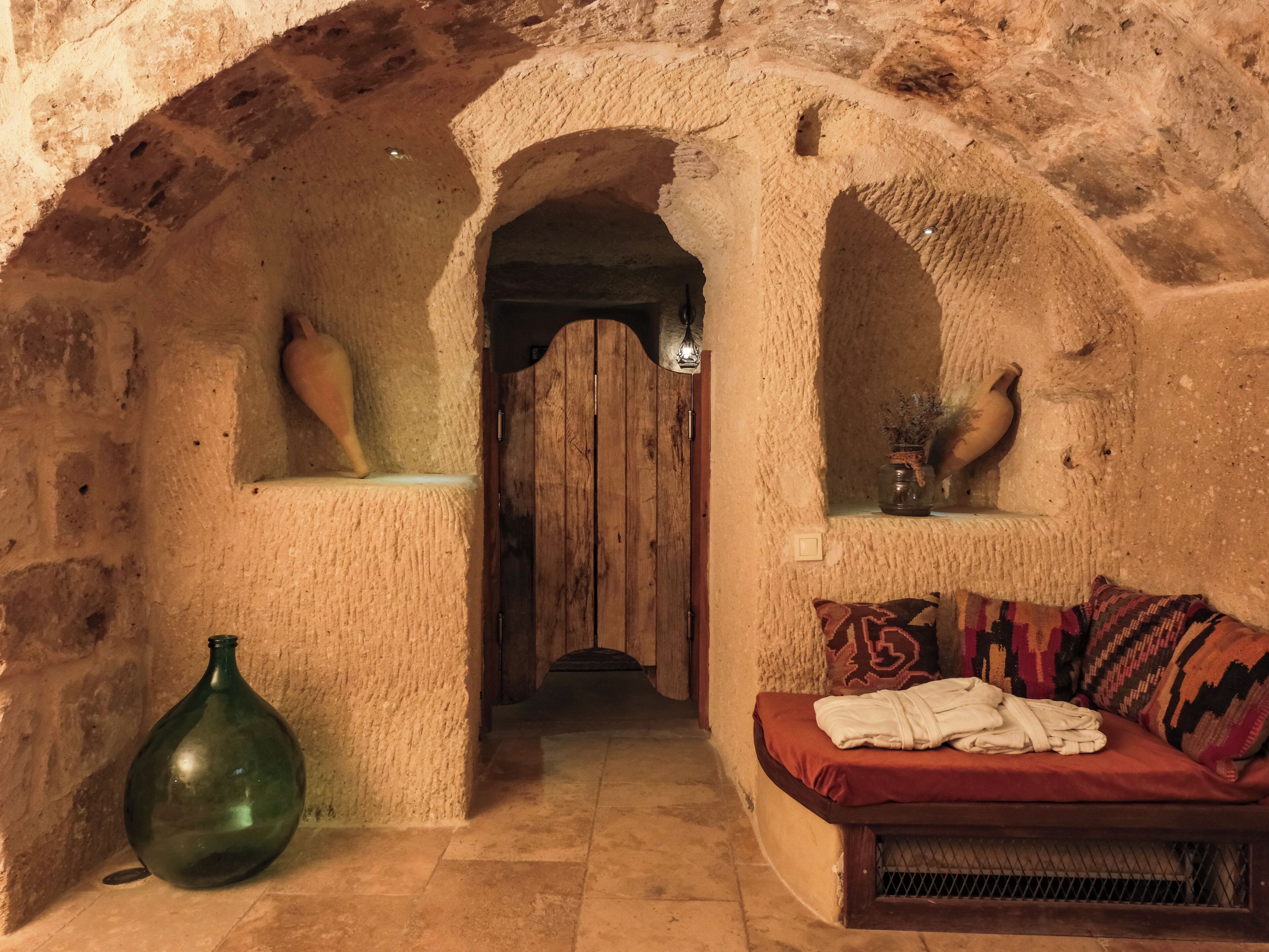 A narrow passageway with a wooden door, a green vase, and a sofa with patterned cushions.