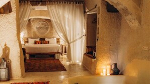 Una habitación con paredes de piedra, una cama, un tapete rojo con estampado y una bañera verde.
