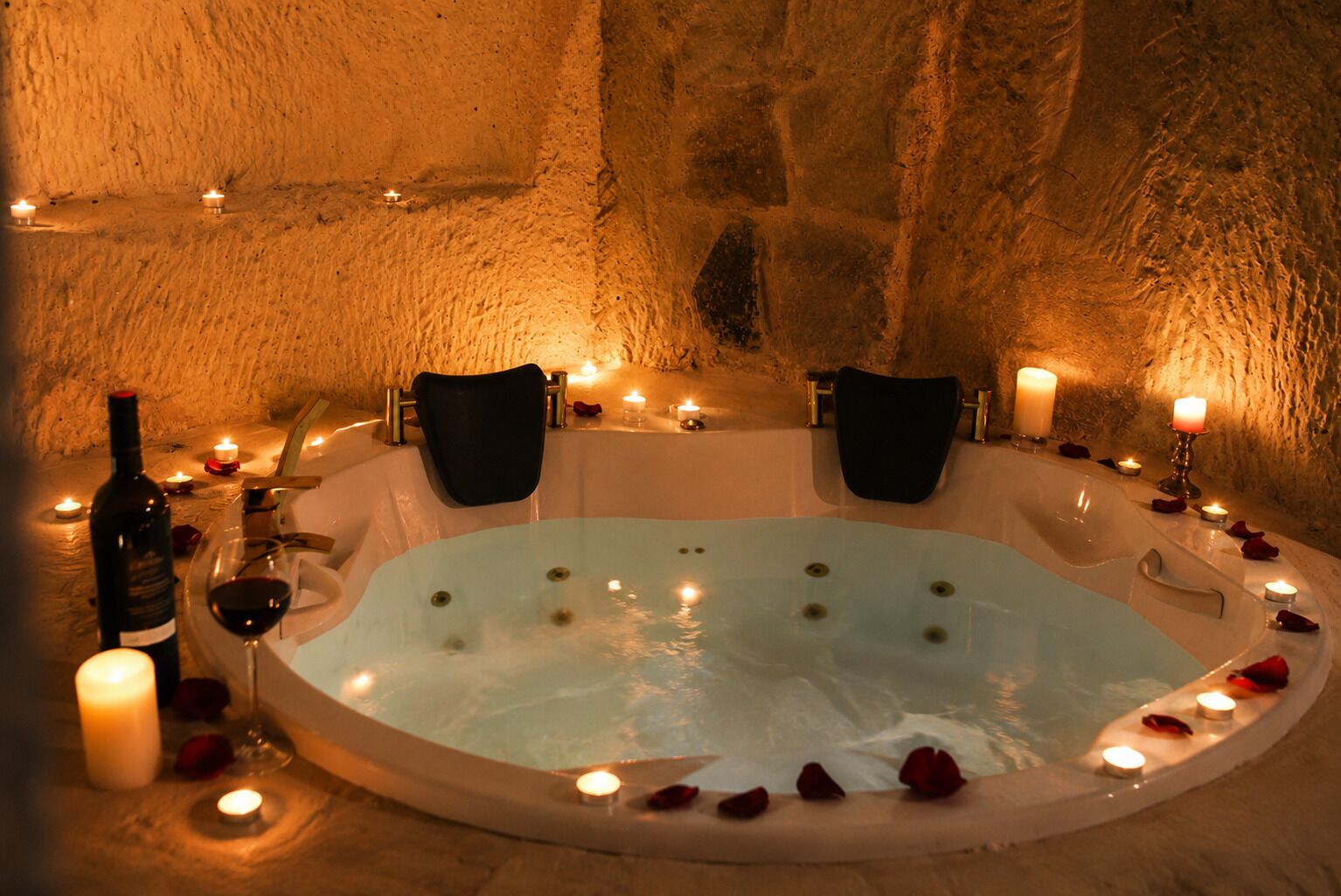 Une pièce aux murs de pierre, dotée d’une grande baignoire, de bougies et de pétales de rose.