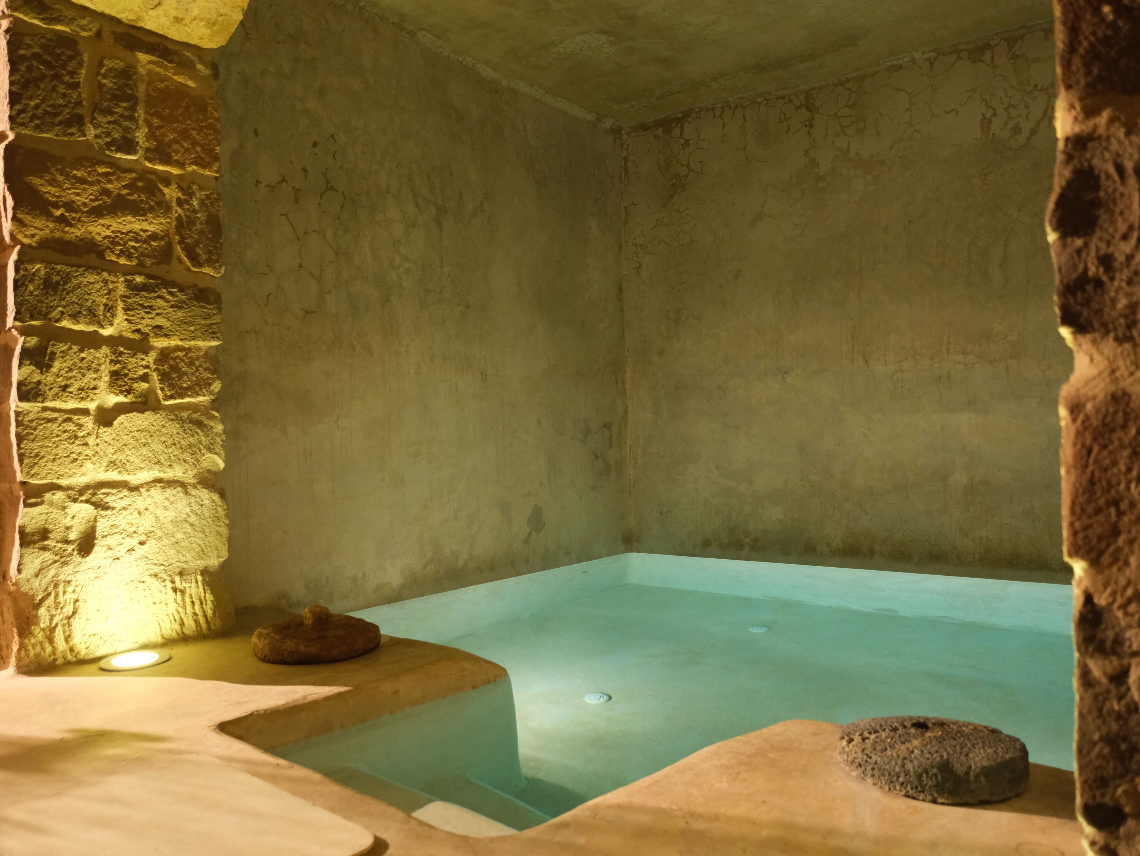 A stone-walled room with a rectangular pool, a stone bench, and a small circular platform.