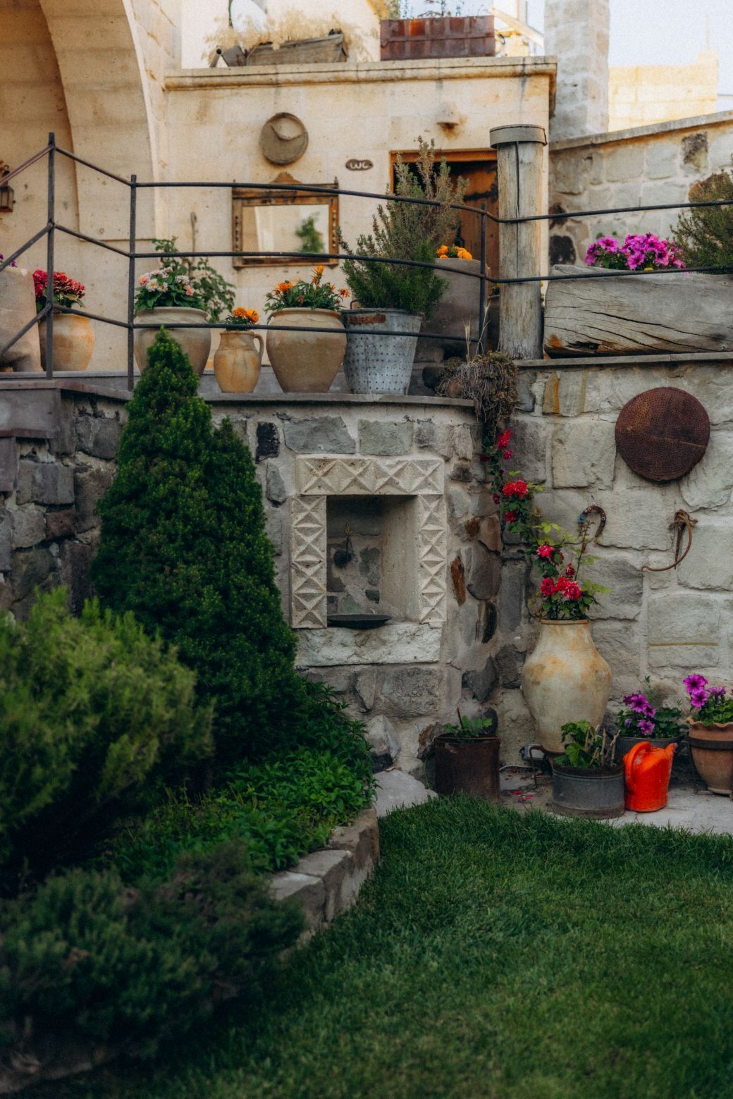 A stone wall with a small window, potted plants, and a metal railing.