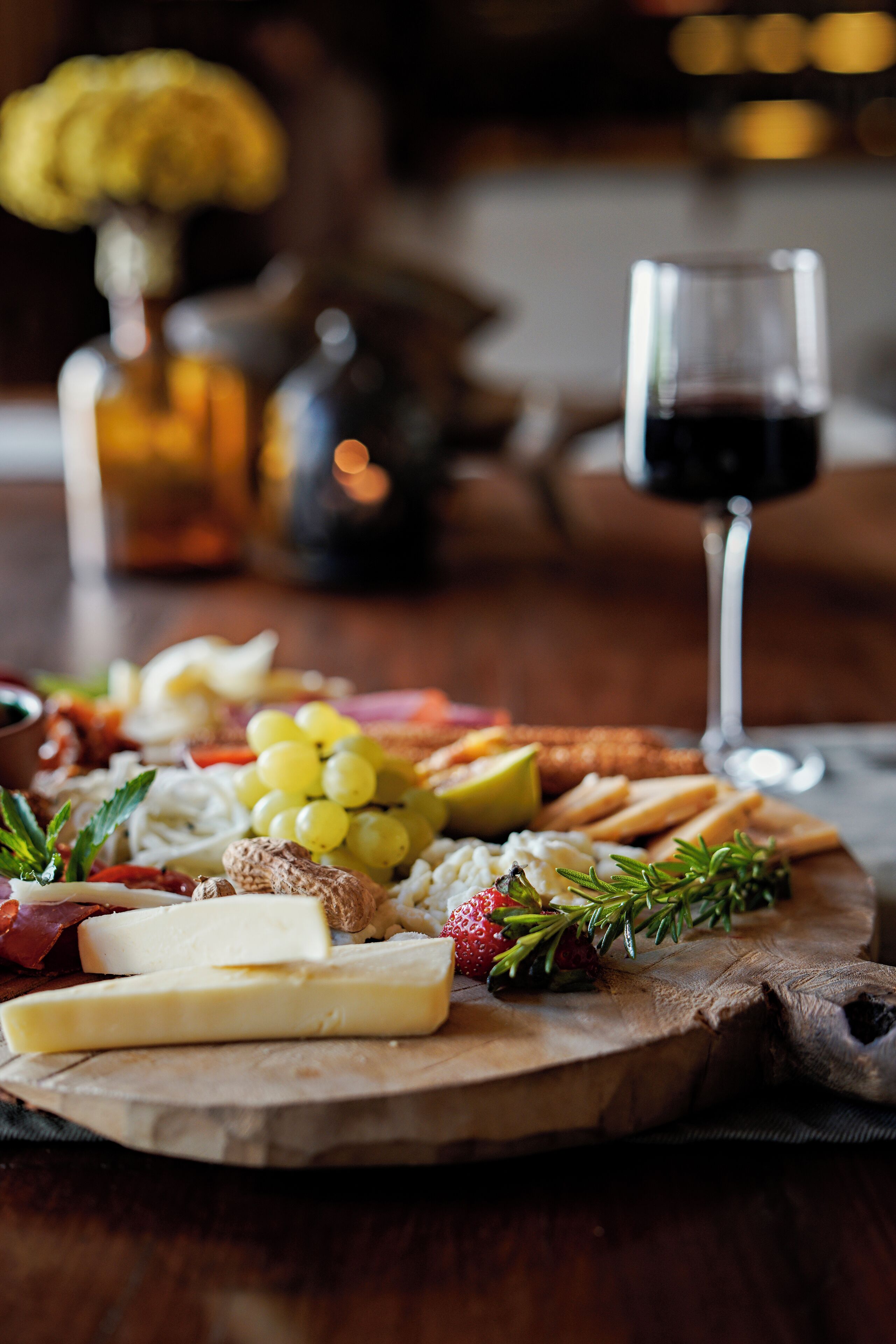 Un tagliere di legno con diversi formaggi, grappe e cracker, accompagnato da un bicchiere di vino rosso.