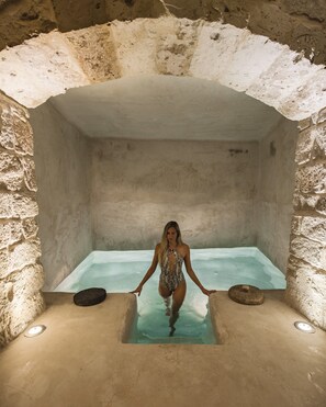 Una persona en una habitación de paredes de piedra con una pequeña piscina.