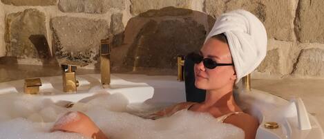 Una persona en un jacuzzi con un muro de piedra al fondo.