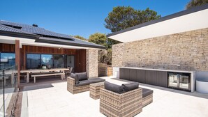 Un espacio exterior moderno con muro de piedra, cerramiento de vidrio y mobiliario exterior.