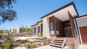 Una casa moderna con fachada de piedra y madera, una terraza de madera y un camino de piedra que lleva a la entrada.