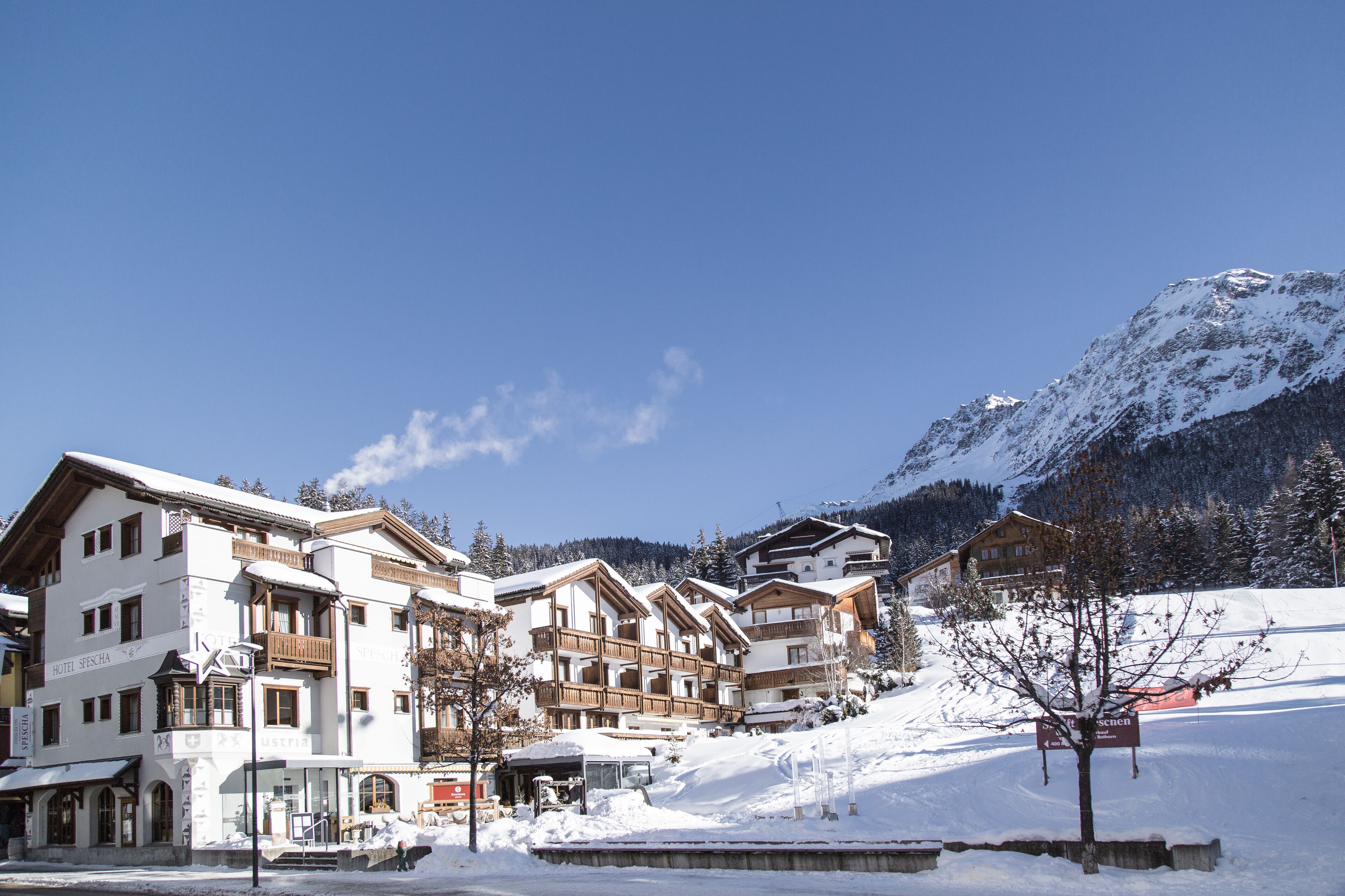 Un hotel con varios pisos, balcones y una montaña nevada al fondo.