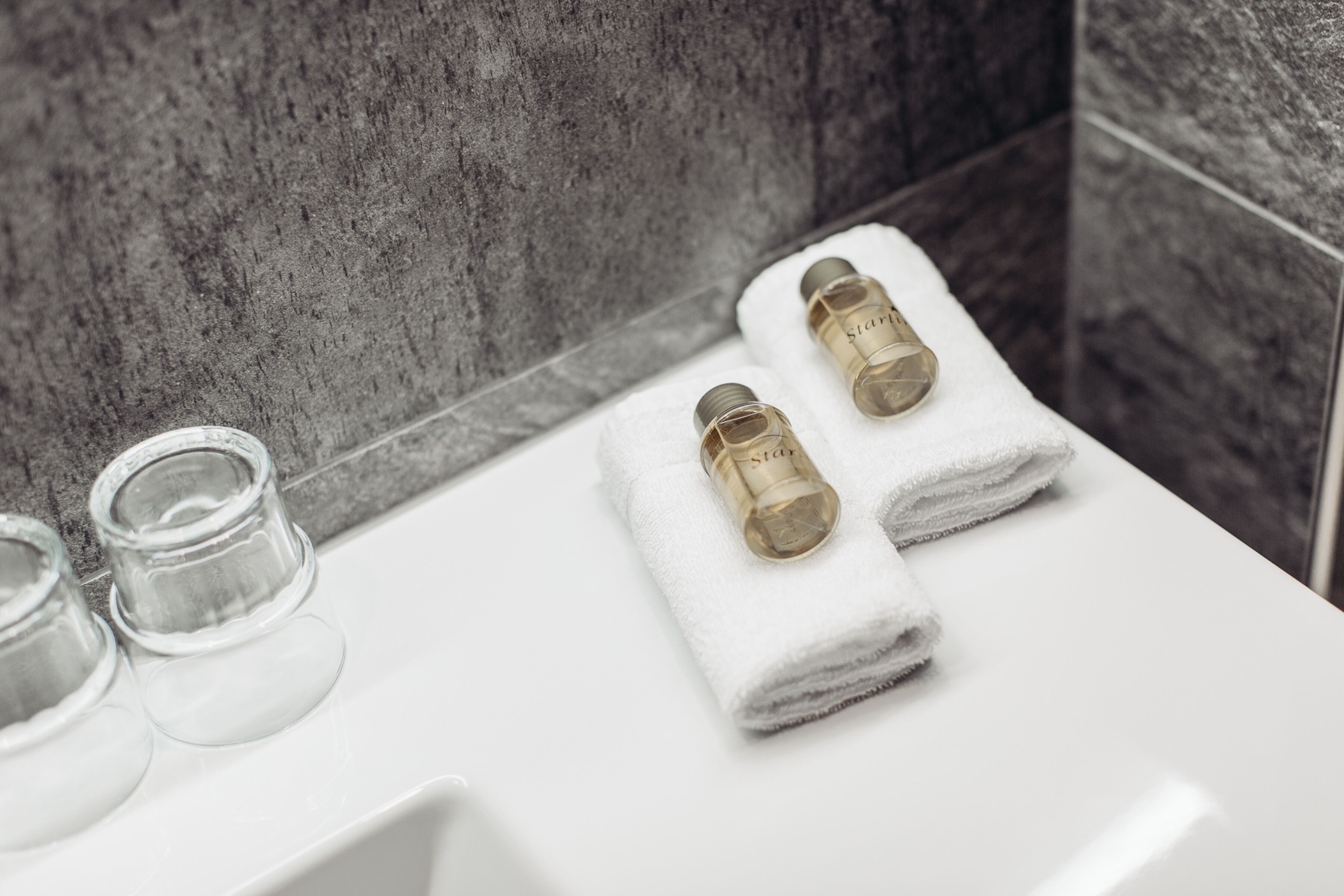 Ein Badezimmer mit einem weißen Waschbecken, zwei Handtüchern und zwei Glasflaschen auf der Ablagefläche.